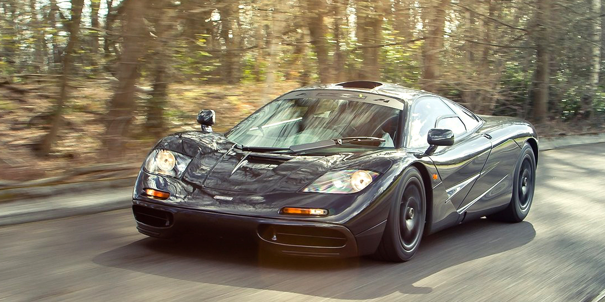A black McLaren F1 driving down a country road