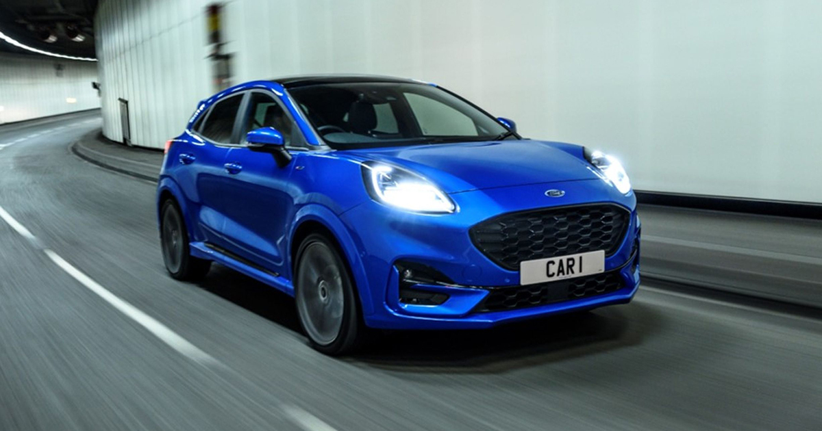 Front angle of a blue Ford Puma driving with its lights on