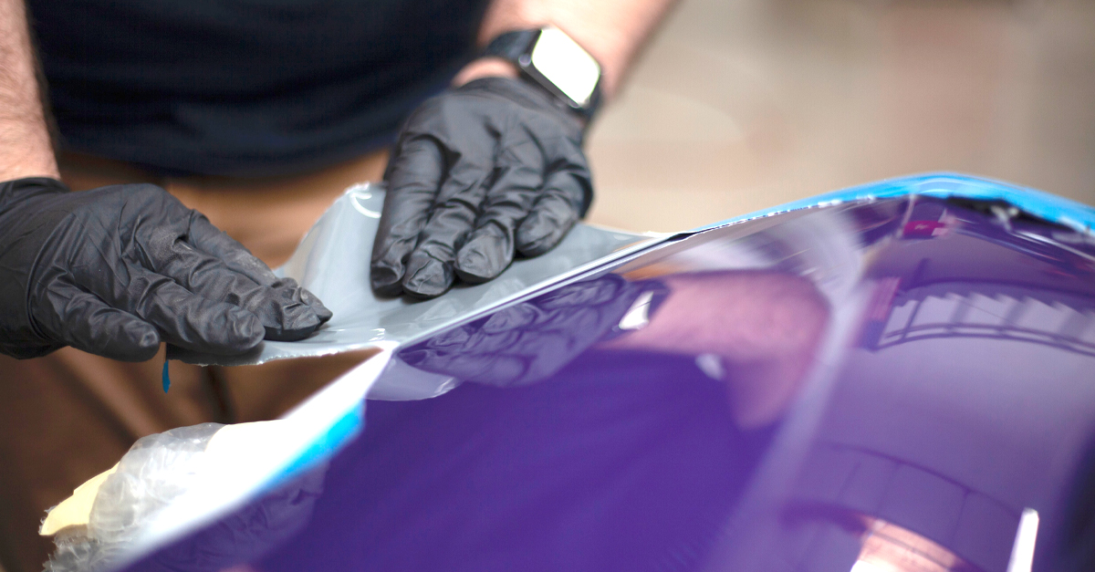 A person wearing black gloves applying paint to a car