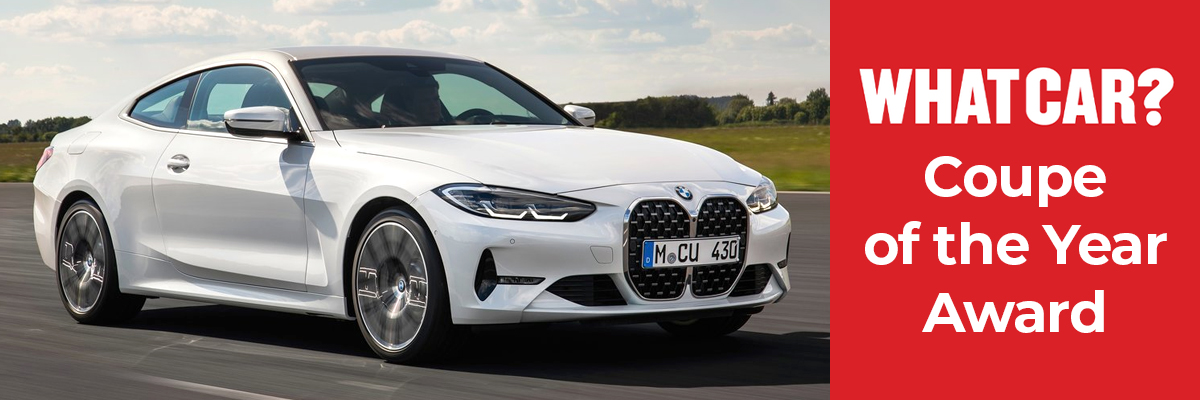 A white BMW 4 Series coupe driving down a country road
