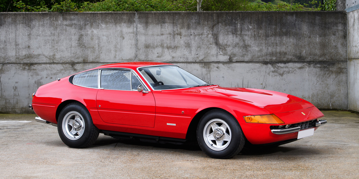 A red Ferrari 365 GTB/4 Daytona parked in front of a concrete wall