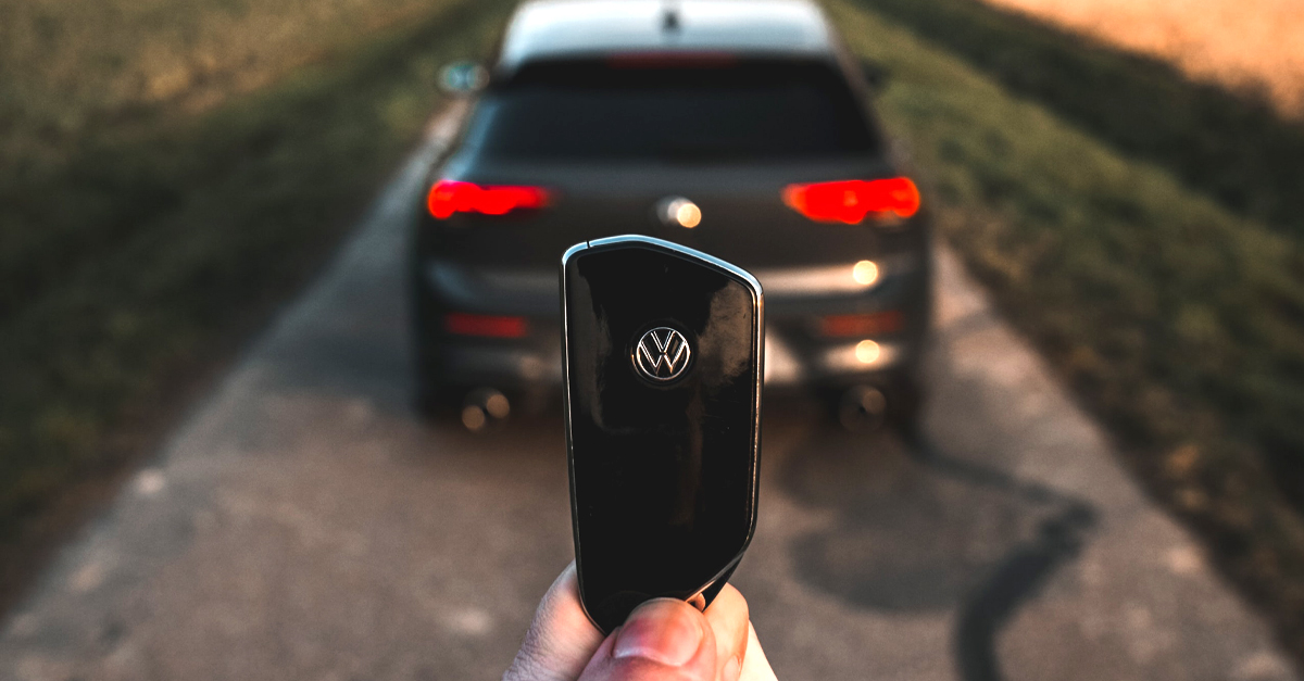 A person holding a car key fob with a car in the background