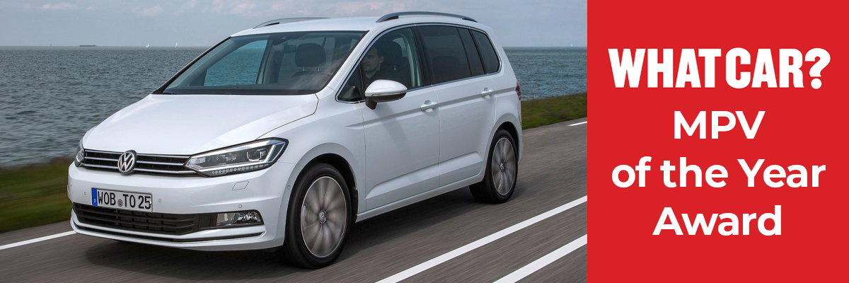 A Volkswagen Touran driving down a road next to the sea