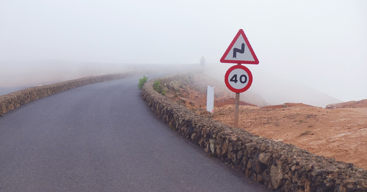 A speed sign next to a foggy country road