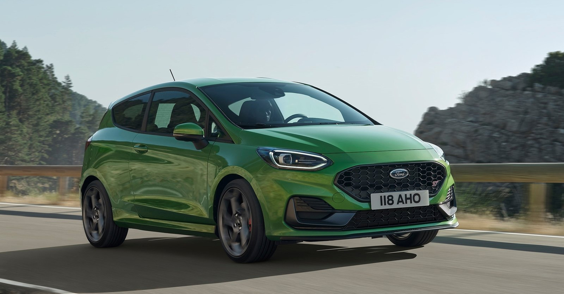 A green Ford Fiesta driving down a road