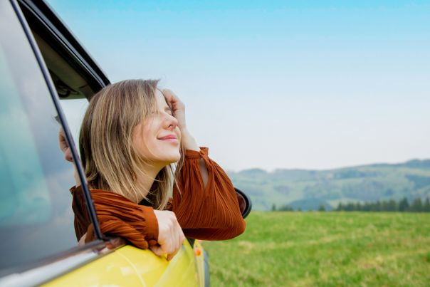 A person with their feet hanging out of the window of a leased vehicle that is parked on the beach.