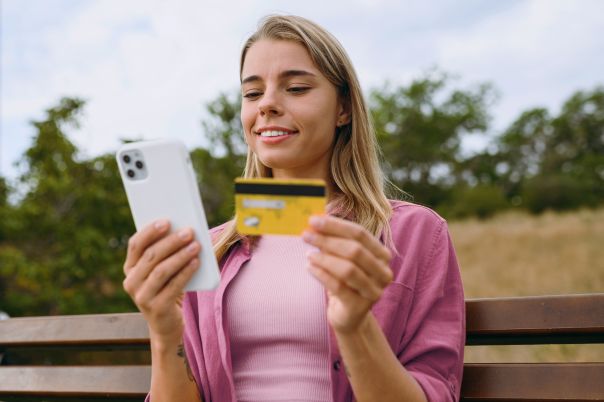 A woman sitting on a bench using her phone and holding a fuel card.